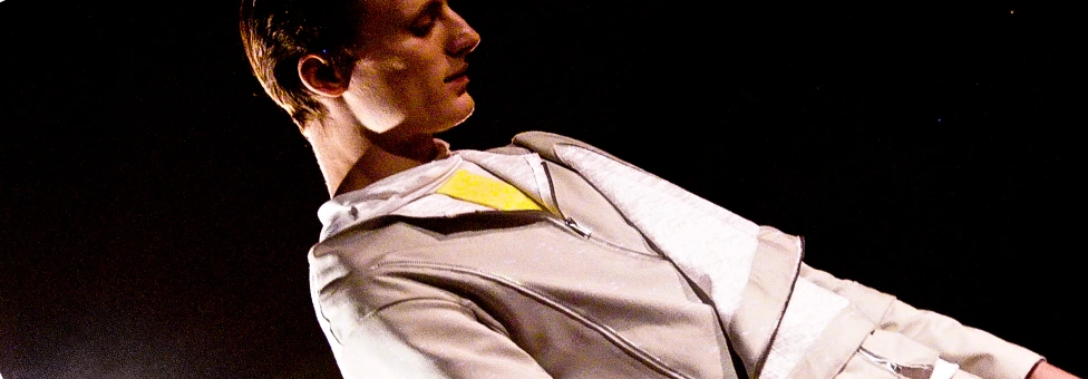 male model on runway wearing minimal futurist suit in grey and white with a yellow stripe